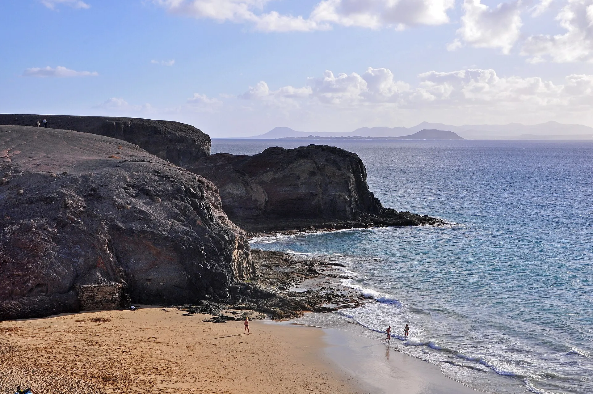 Eine Bucht bei Papagayo, mit dunklen Klippen, goldenem Sand und den Nachbarinseln am Horizont