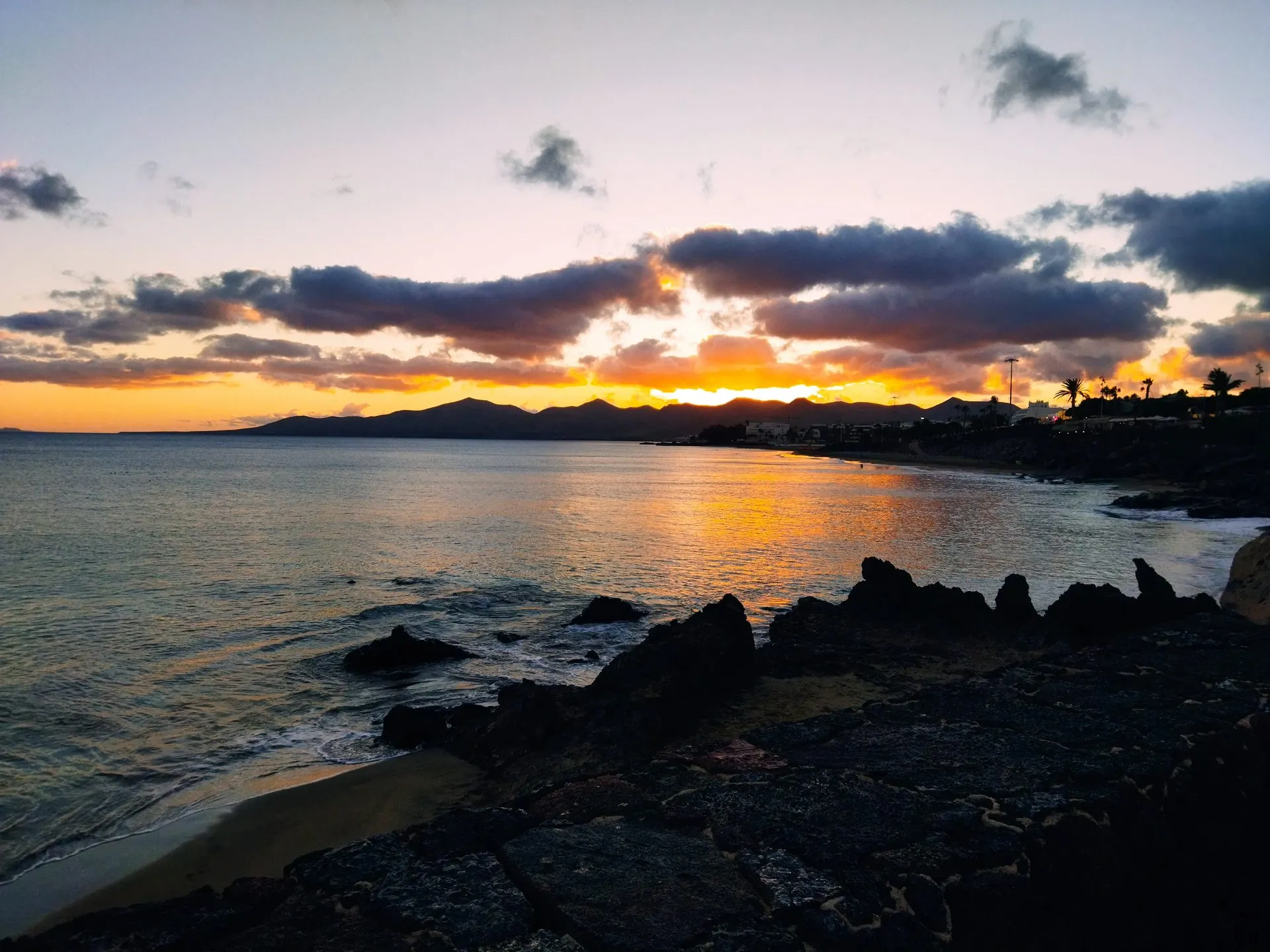 Sunset over Playa Grande in Puerto del Carmen, with lava rocks in the foreground