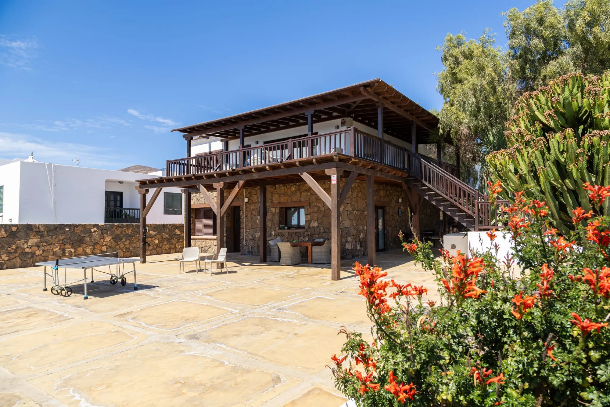 The house from the courtyard: the timber terrace over the stone ground floor, with flowers in the foreground